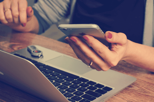 A person checking their phone while sitting in front of their laptop. 