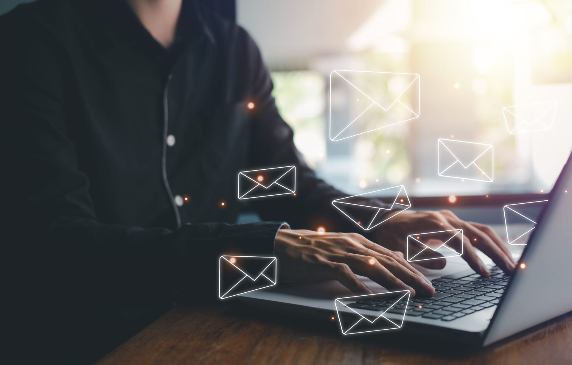 A person uses a laptop surrounded by holographic email icons.
